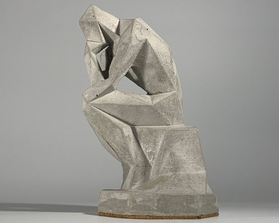 A faceted concrete statue of a seated thinking figure
